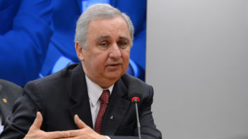 #pracegover Pecuarista José Carlos Bumlai sentado, de terno azul escuro e gravata vermelha, falando ao microfone e encostando as mãos.