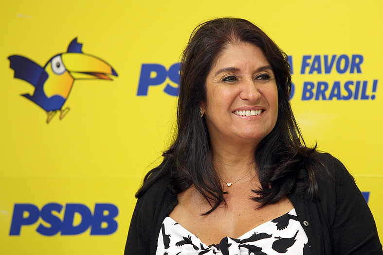 #pracegover foto mostra Thelma de Oliveira sorrindo e atrás com fundo com PSDB e um tucano
