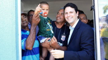 #pracegover: ministro Bruno Araújo ao lado de um senhor com uma criança no colo entregando moradia