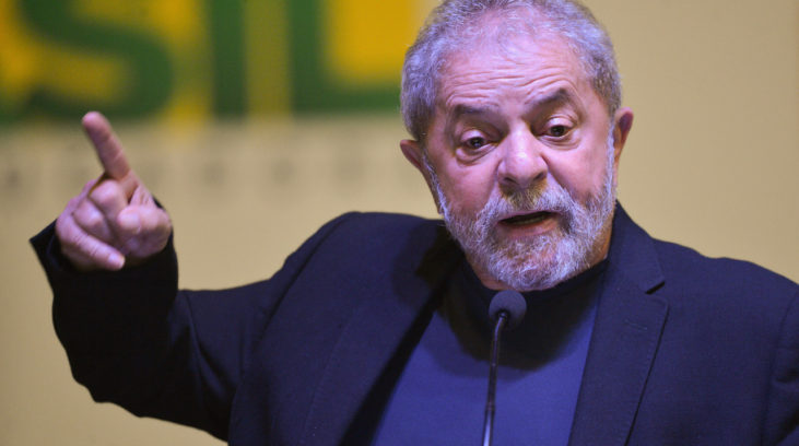 #pracegover Ex-presidente Lula está com paletó e blusa azul e com dedo indicador do lado direito apontado