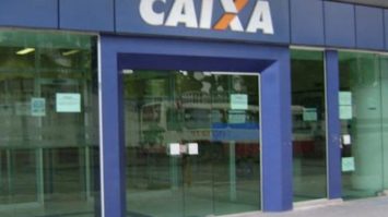 #pracegover: foto mostra fachada de uma agência da Caixa Econômica Federal em azul com o nome do banco em destaque CAIXA