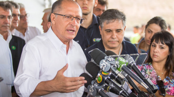 #pracegover: foto mostra governador de São Paulo, Geraldo Alckmin, falando de frente a um púlpito cheio de microfones. Tucano está de camisa social branca, rodeado por pessoas