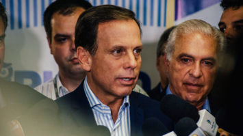 #pracegover: foto mostra prefeito da cidade de São Paulo, João Doria (PSDB), concedendo entrevista e rodeado de secretários, vice-prefeito e jornalistas