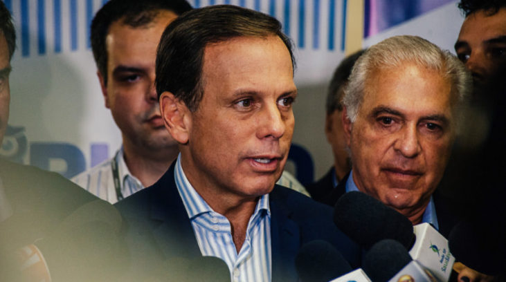 #pracegover: foto mostra prefeito da cidade de São Paulo, João Doria (PSDB), concedendo entrevista e rodeado de secretários, vice-prefeito e jornalistas