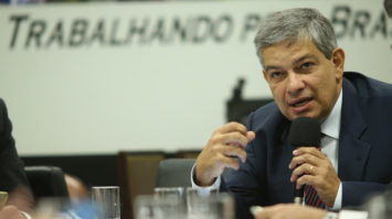 #pracegover: Marcus Pestana está sentado, gesticulando com a mão direita e segurando a mão esquerda