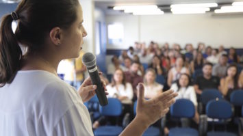 #pracegover: prefeita Raquel Lyra está de costas, falando ao microfone para plateia formada por professores