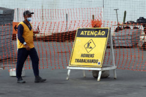 #pracegover: foto mostra obras sendo feitas em aeroporto de Salvador. Tem um operário andando na pista de Salvador e uma placa amarela e preta com "Atenção, homens trabalhando"