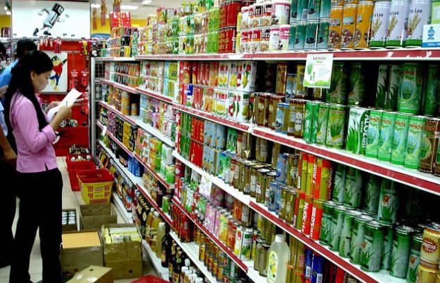 #pracegover: foto mostra mulher olhando lista de compras em corredor de supermercado