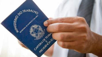 #pracegover: foto mostra carteira de trabalho em close, sendo aberta por uma pessoa