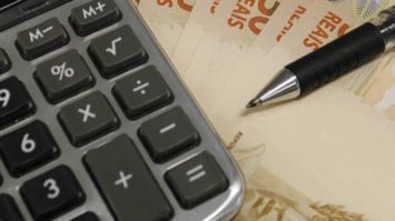 #pracegover: foto mostra calculadora e caneta em cima de três notas de R$50