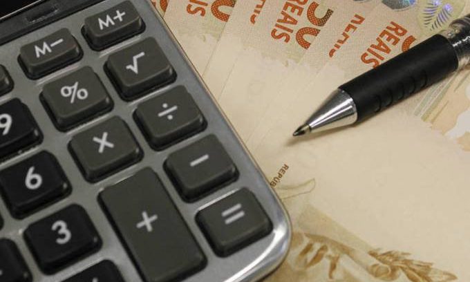 #pracegover: foto mostra calculadora e caneta em cima de três notas de R$50