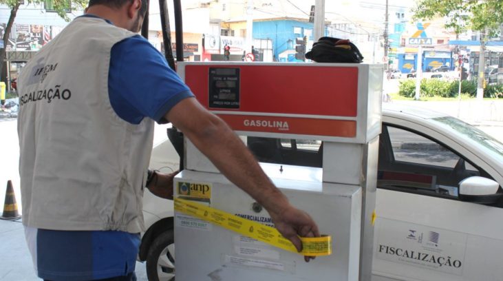 #pracegover: foto mostra fiscal passando fita amarela interditando posto de combustível