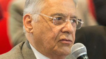 #pracegover: foto de perfil do ex-presidente FHC segurando microfone e vestindo paletó marrom, blusa branca, óculos e gravata