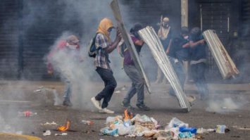 #pracegover: foto mostra manifestantes com rostos cobertos segurando placas e paus em protesto na Venezuela