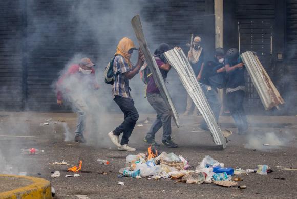 #pracegover: foto mostra manifestantes com rostos cobertos segurando placas e paus em protesto na Venezuela
