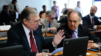 #pracegover: foto mostra o senador Tasso Jereissati sentado gesticulando com a mão esquerda e na outra segurando um papel em frente ao laptop