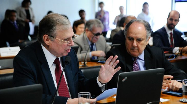 #pracegover: foto mostra o senador Tasso Jereissati sentado gesticulando com a mão esquerda e na outra segurando um papel em frente ao laptop
